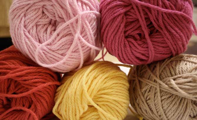 Five balls of yarn in shades of pink and red.