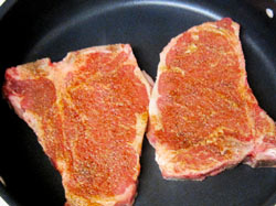 Two T-Bone steaks being seared in a non-stick skillet